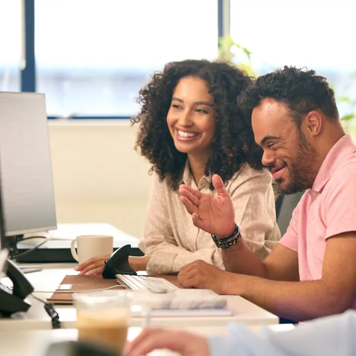 Disabled man with down syndrome sitting at desk with support worker, both smiling