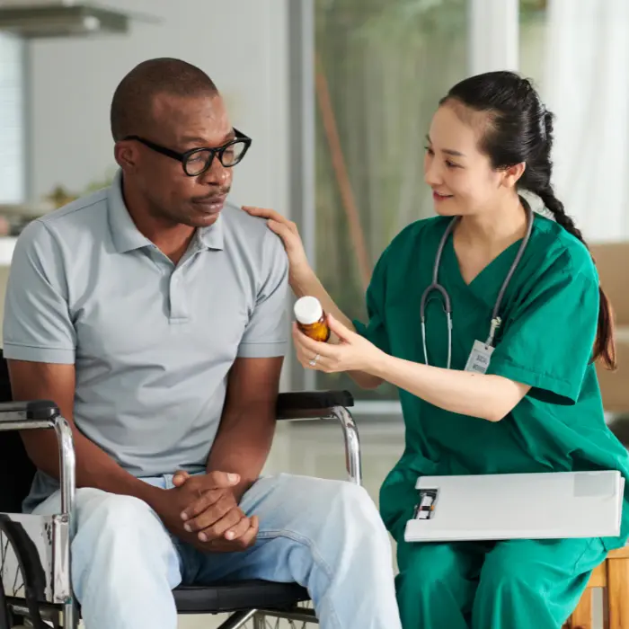 Disabled man in wheelchair in home with community nurse looking at medication together