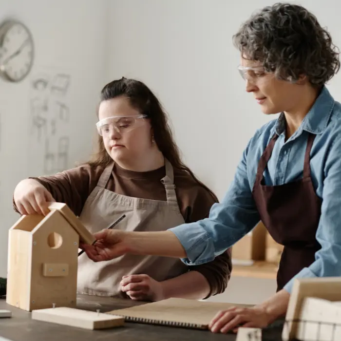 Support worker with disabled girl with down syndrome in a building workshop class